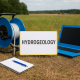 Matériel d'hydrogéologie en plein champ : ordinateur portable, carnet, sonde et panneau indiquant 'Hydrogeology